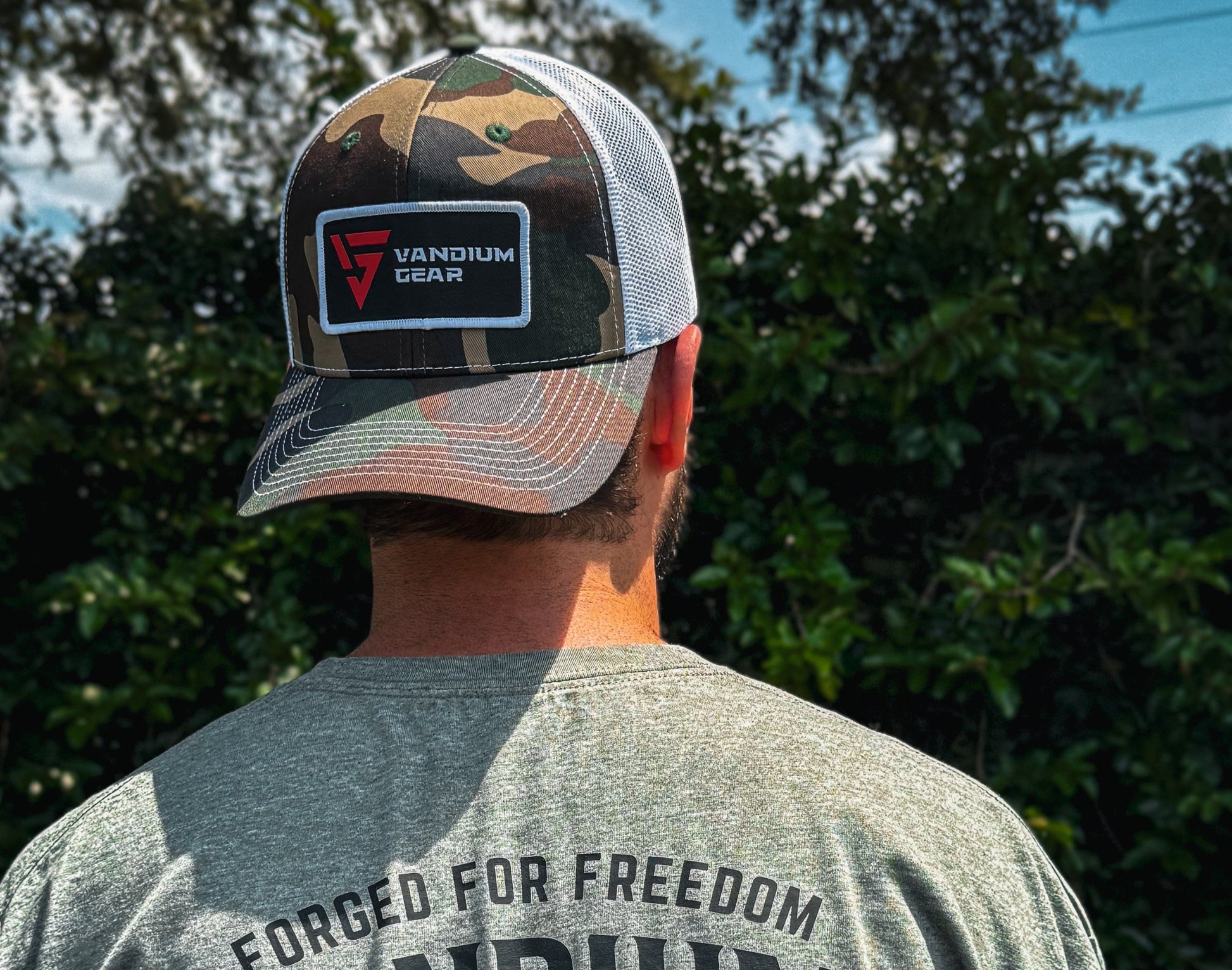 Person wearing a cap and 'Vandium Gear' t-shirt with an eagle design outdoors.